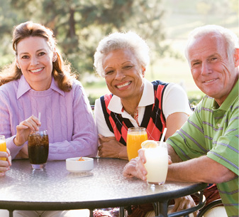 senior man senior woman and young woman sitting at a table with drinks in hand