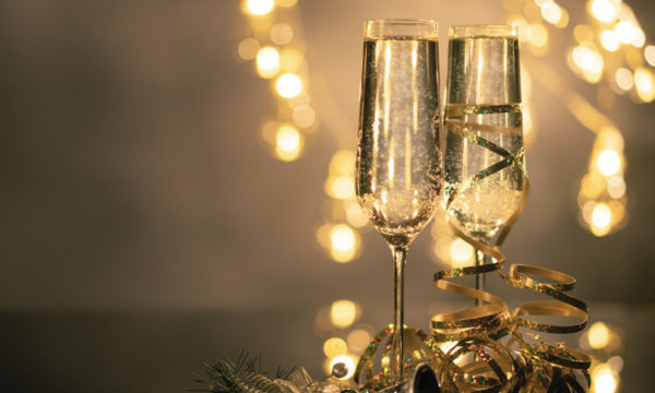 two champagne flutes sitting on table in focus while christmas lights in background out of focus
