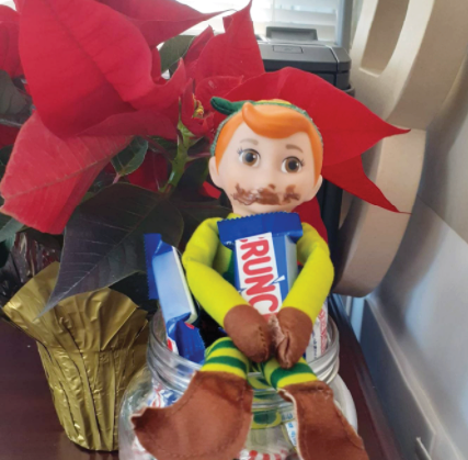 toy elf sitting in candy jar eating a Crunch chocolate bar