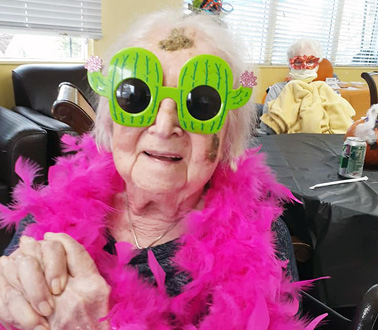senior woman dressed up for Halloween with bright green sunglasses and a bright pink boa