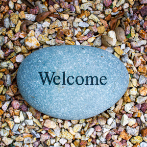 stock image from Canva of a stone laying on multi color pebbles. Main stone in center has WELCOME carved into it.