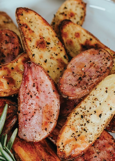 Seasoned crispy potatoes plated on a white dish with rosemary sprigs
